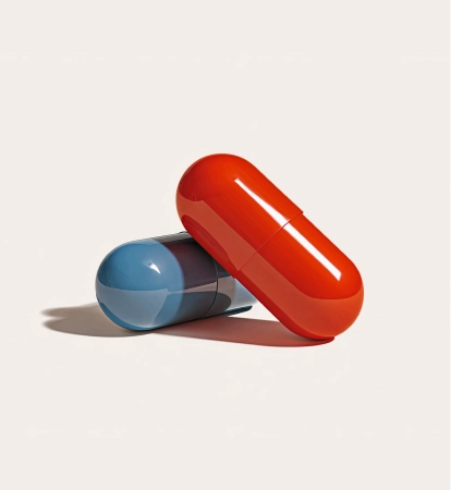 Two large glossy capsules, one red and one blue, resting on a light surface casting shadows.