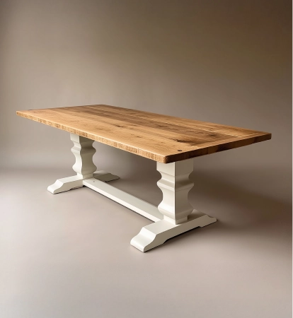Rectangular wooden dining table with a natural wood top and white painted carved pedestal legs connected by a horizontal beam.